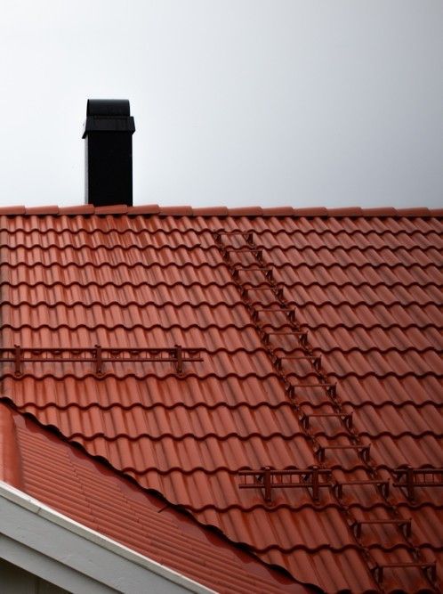 Red tiled roof with a black chimney against a light sky