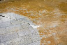 Roof being pressure-washed, with a white cleaning spray on brown-stained shingles.