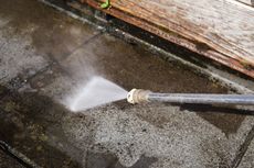 Pressure washer spraying water across a dirty concrete surface outdoors