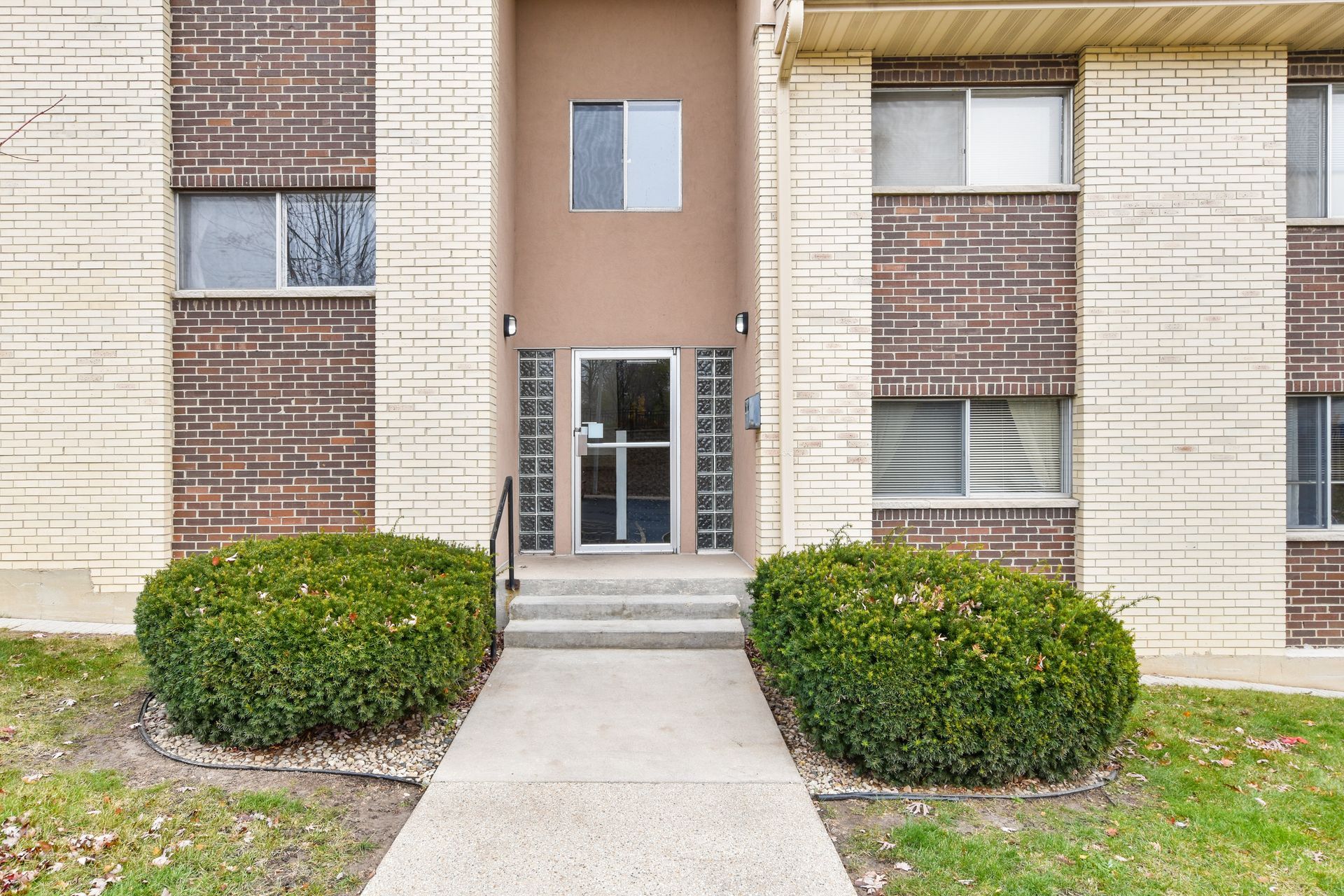 A brick apartment building with a concrete walkway leading to the entrance.