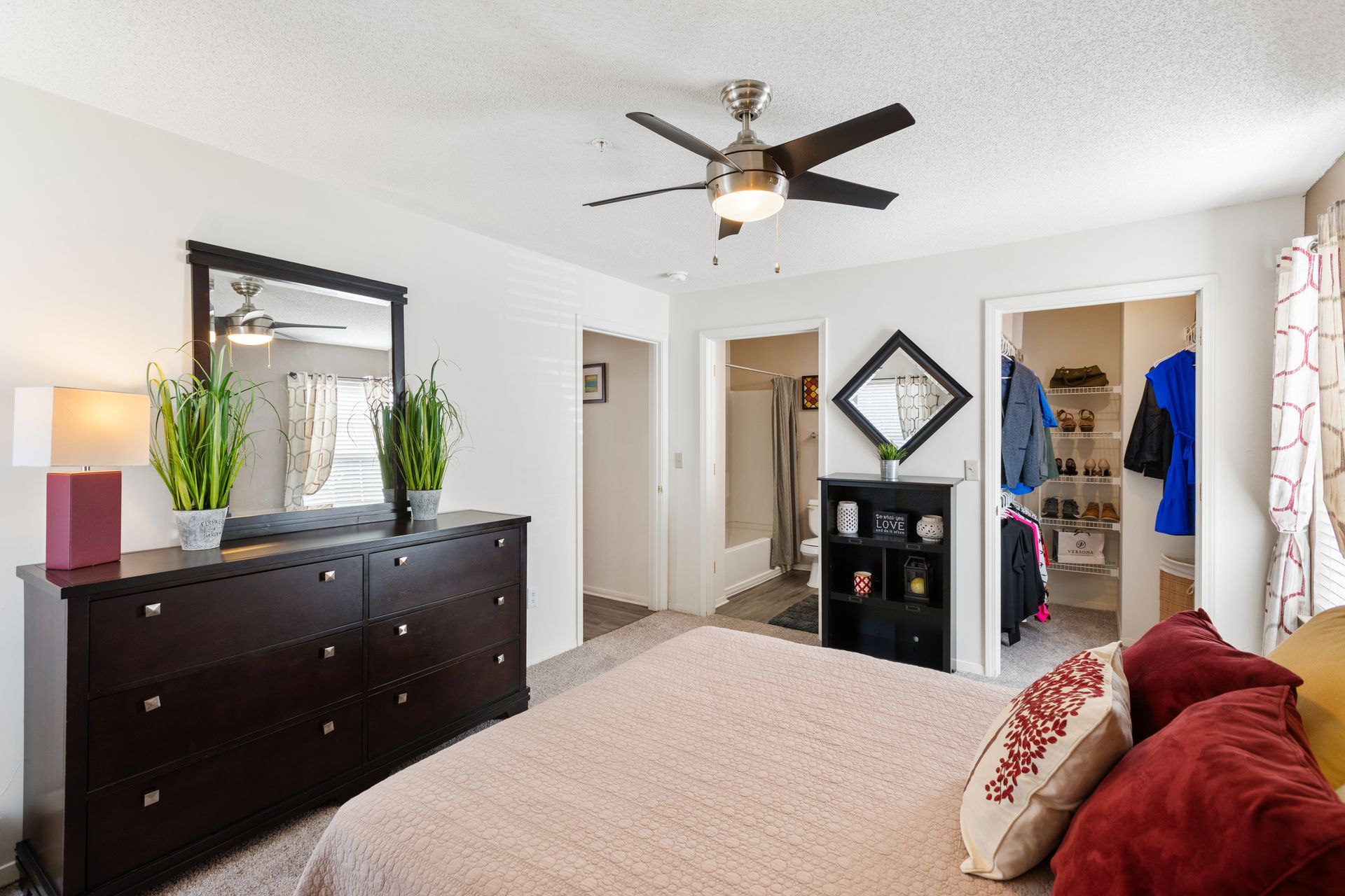 A bedroom with a bed , dresser , mirror and ceiling fan.