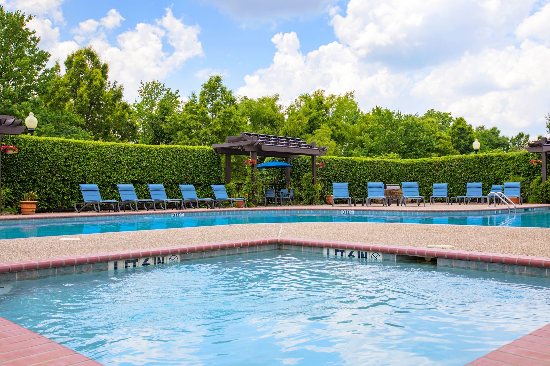 A large swimming pool surrounded by chairs and a pergola