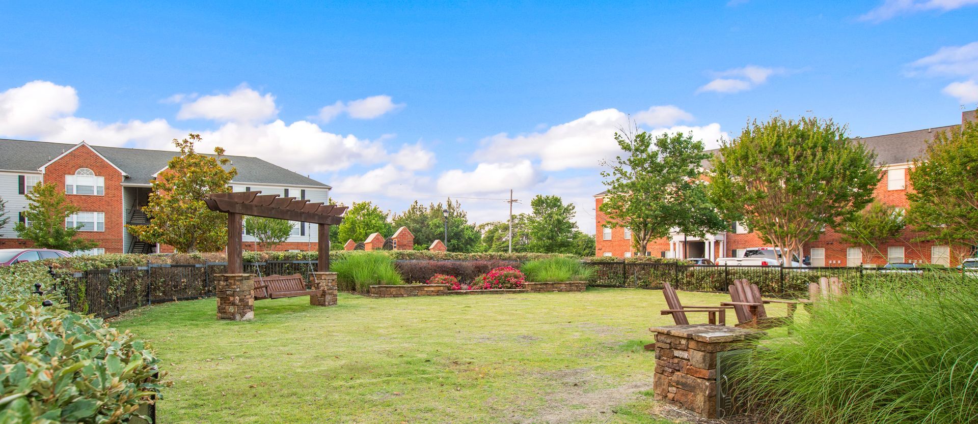 A large grassy field with a picnic table and chairs in front of a brick building.