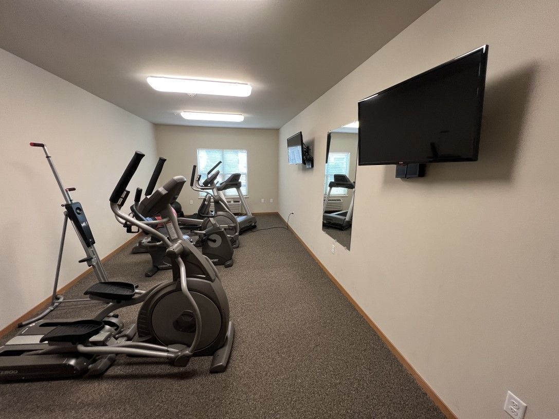 A gym with a lot of exercise equipment and a flat screen tv on the wall.