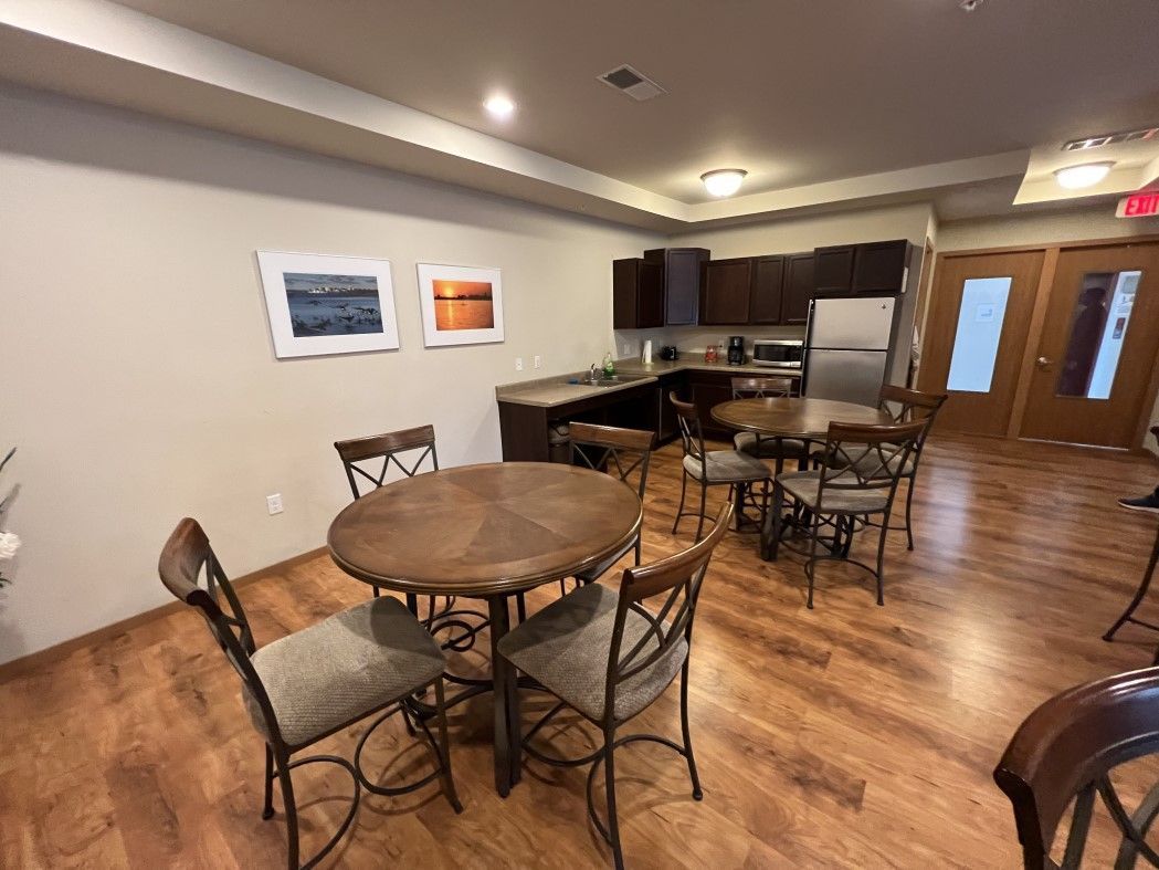 A room with tables and chairs in it and a kitchen in the background.