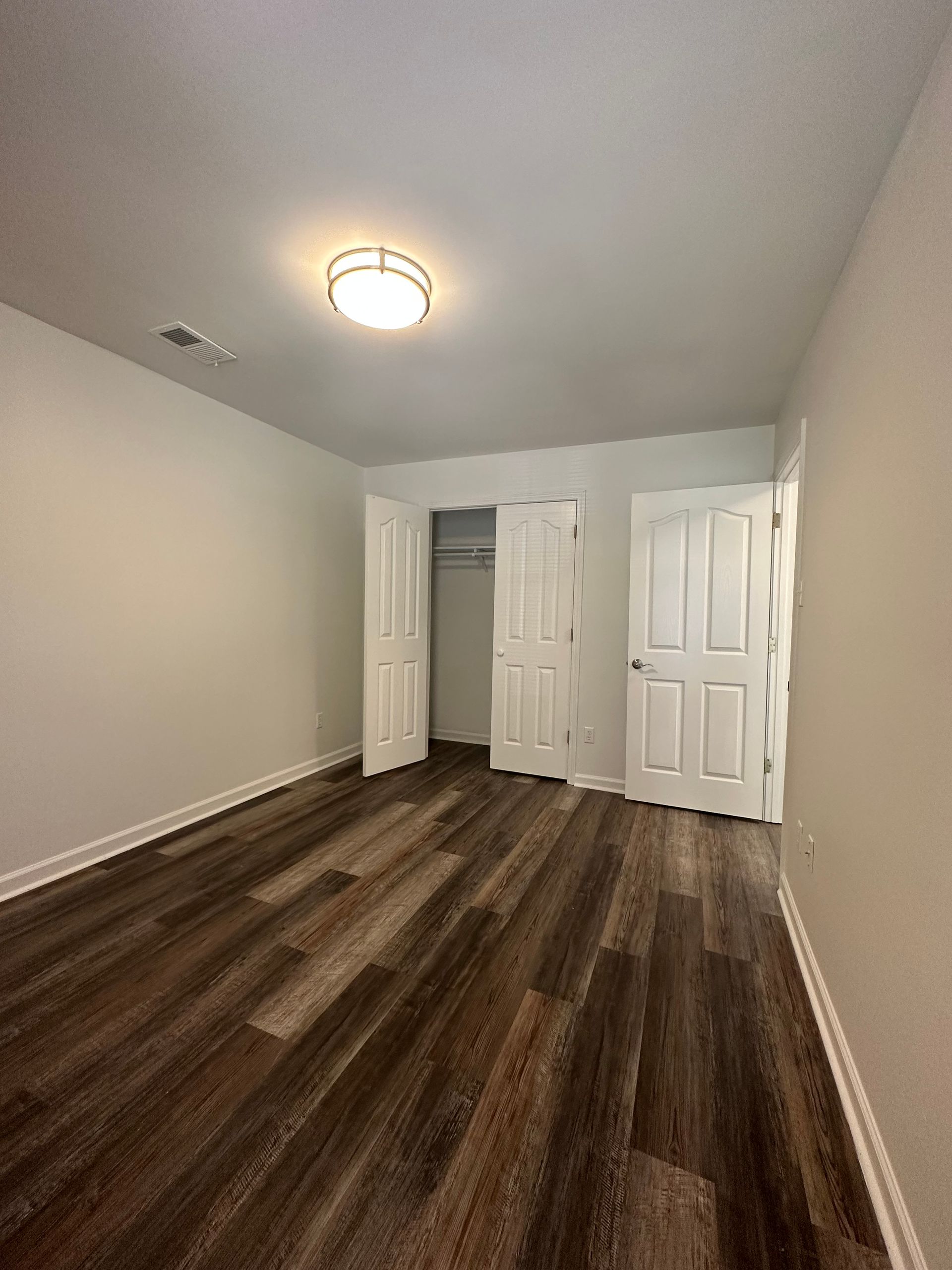 An empty bedroom with hardwood floors and white walls.