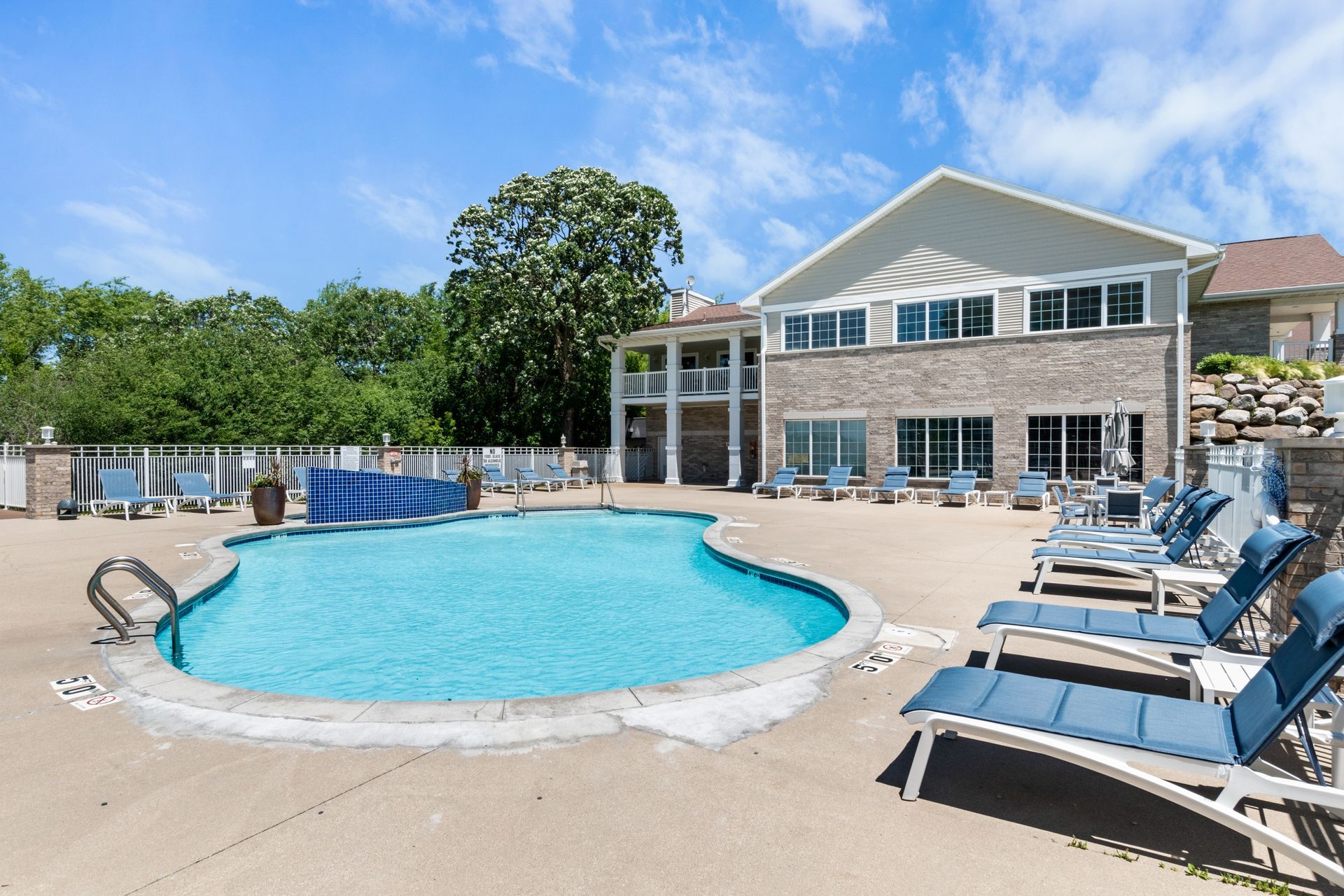 A large swimming pool surrounded by lounge chairs in front of a large house.