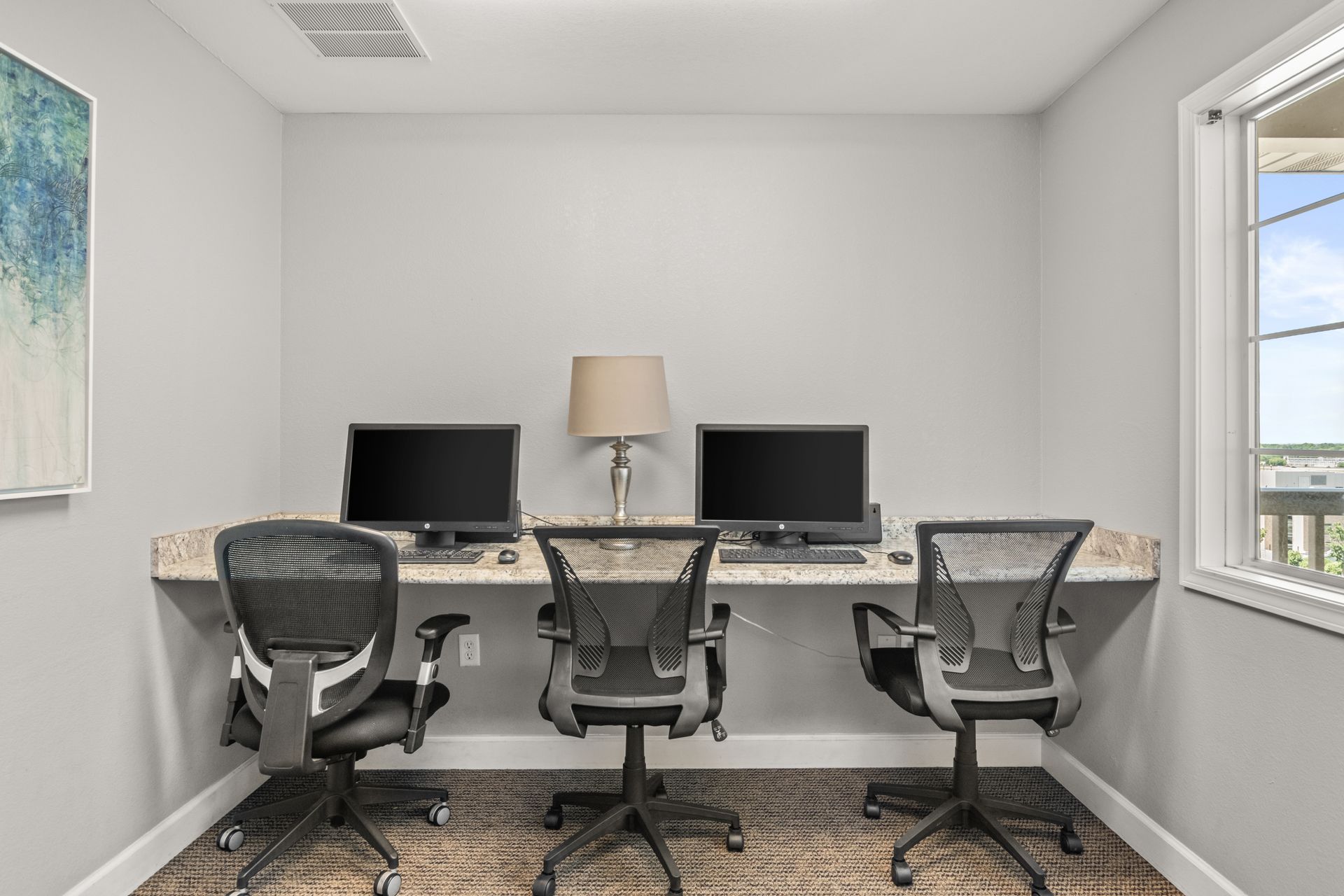 A room with three desks and three chairs with computers on them.