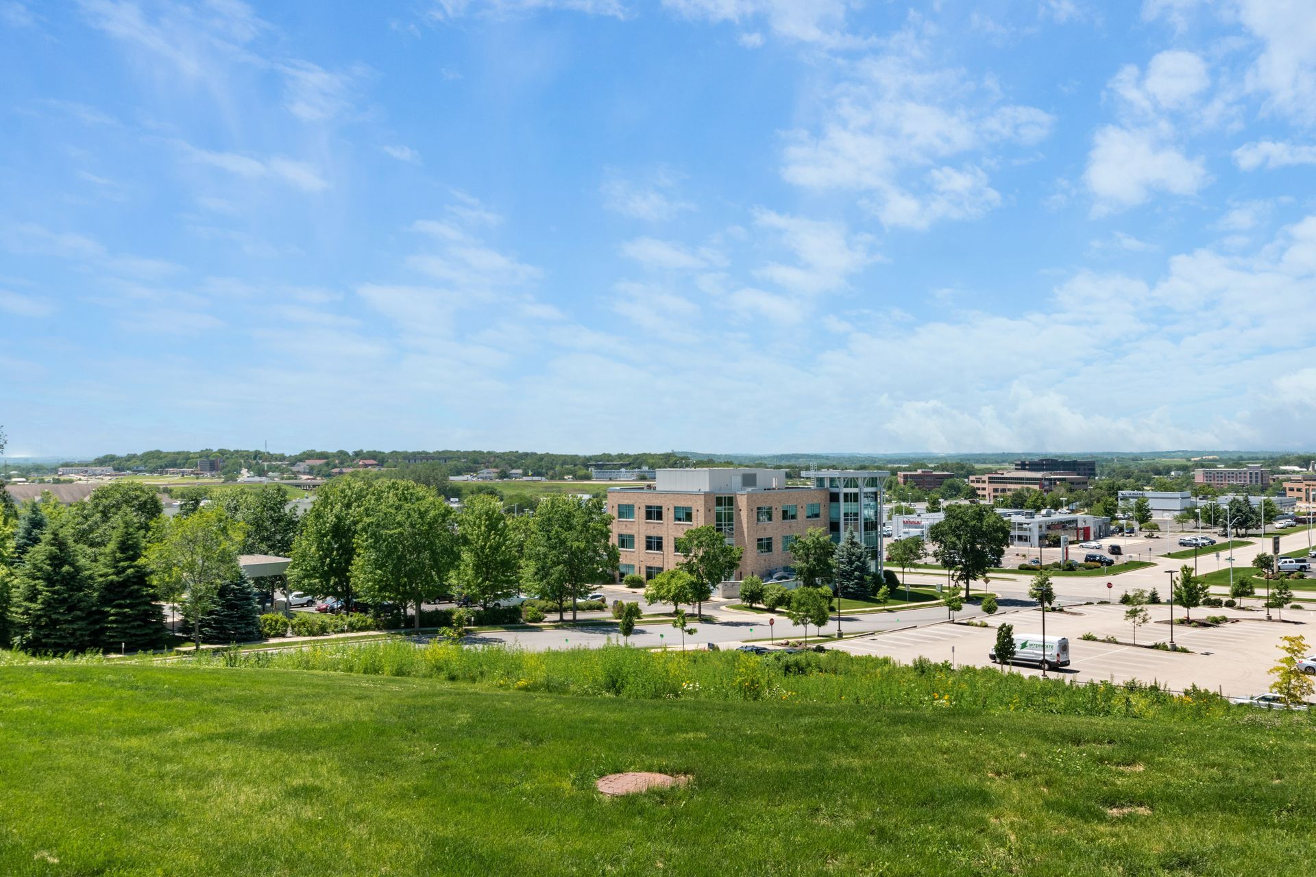 An aerial view of a city with a large grassy field in the foreground and buildings in the background.