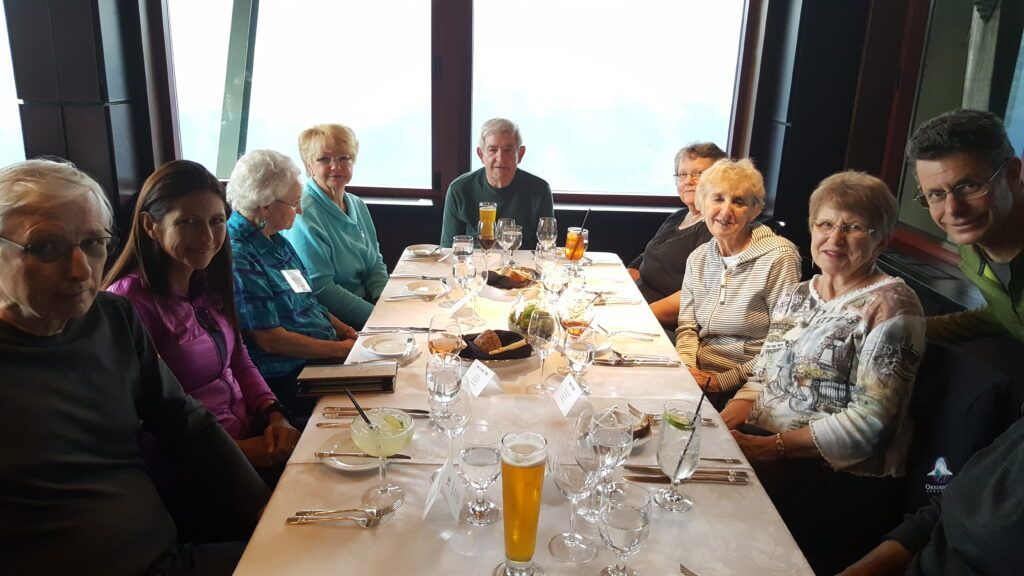People seated around a long dining table with drinks and plates in a bright restaurant.