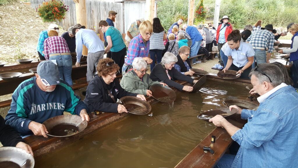 People leaning over a large indoor fish tank, feeding or handling fish at a wooden edge.