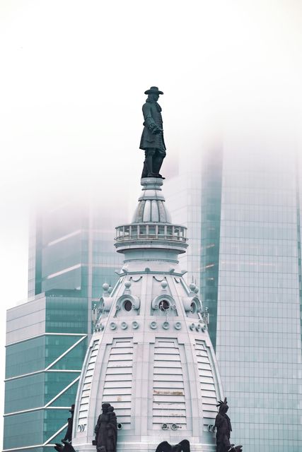Statue atop a white ornate tower in fog, with modern skyscrapers in the background