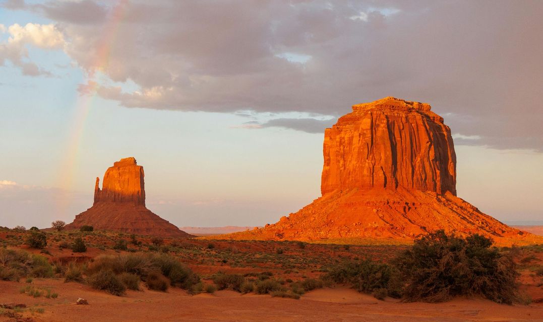 Sunset-lit red sandstone buttes in a desert landscape with a cloudy sky