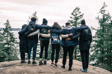 Group of hikers with arms around each other on a rocky overlook in a forest under cloudy skies
