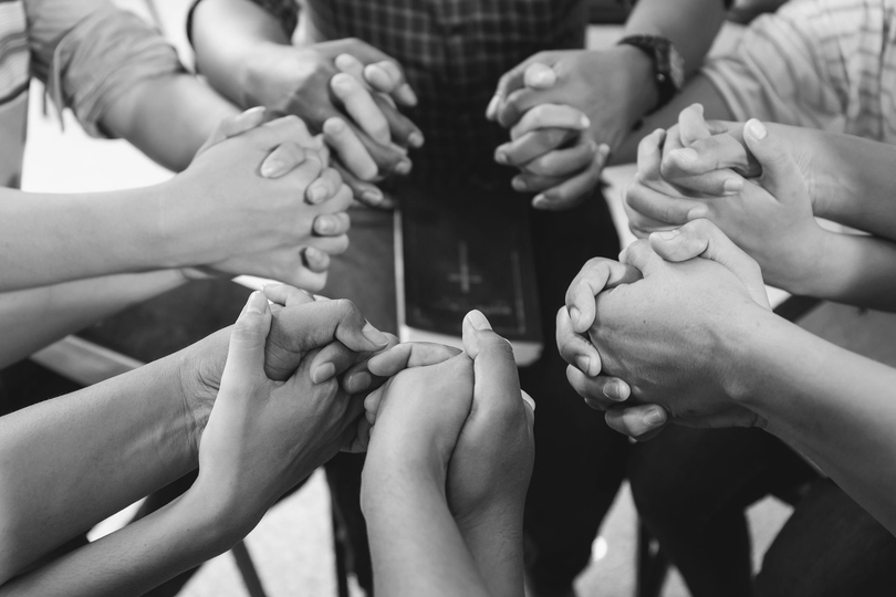 Hands joined together in a circle, black-and-white close-up of teamwork and unity