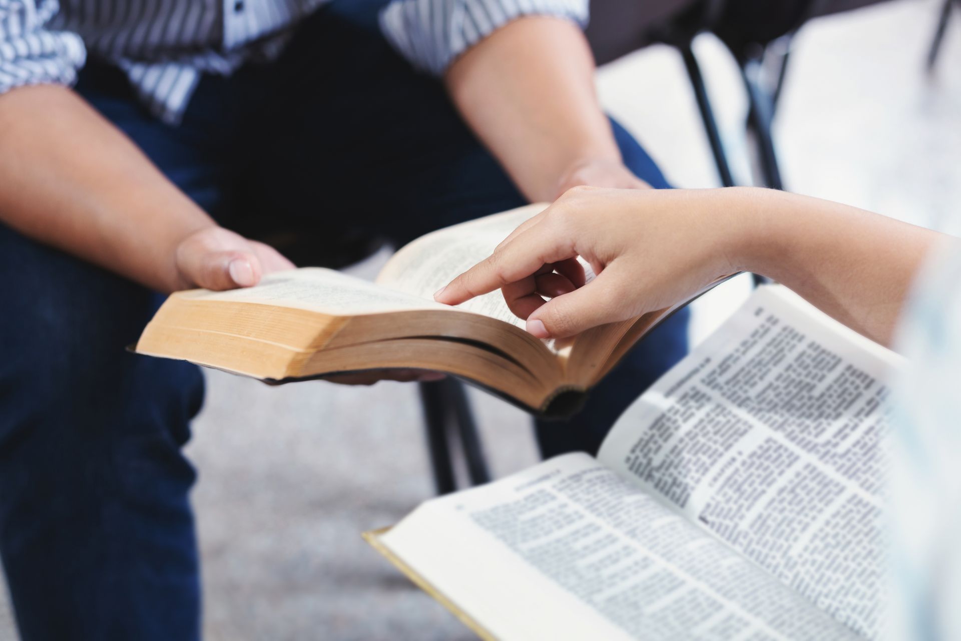 Hands holding open books, one person pointing to a page during a reading discussion