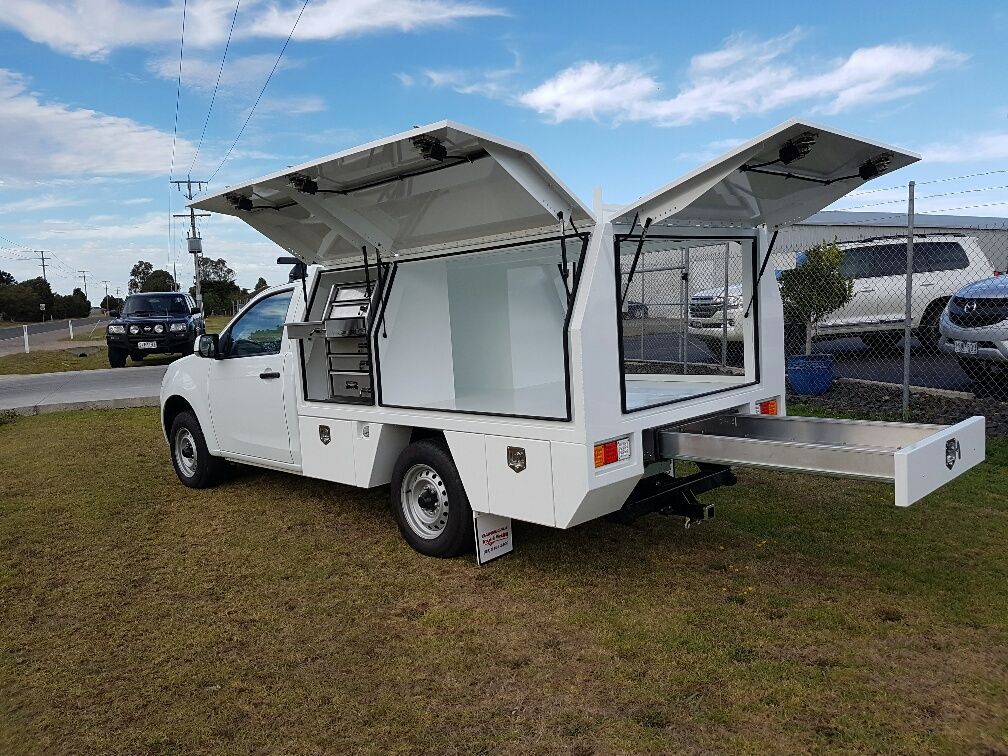 White truck with canopy, doors open, pull-out drawer. Outdoors on grass, cloudy sky.