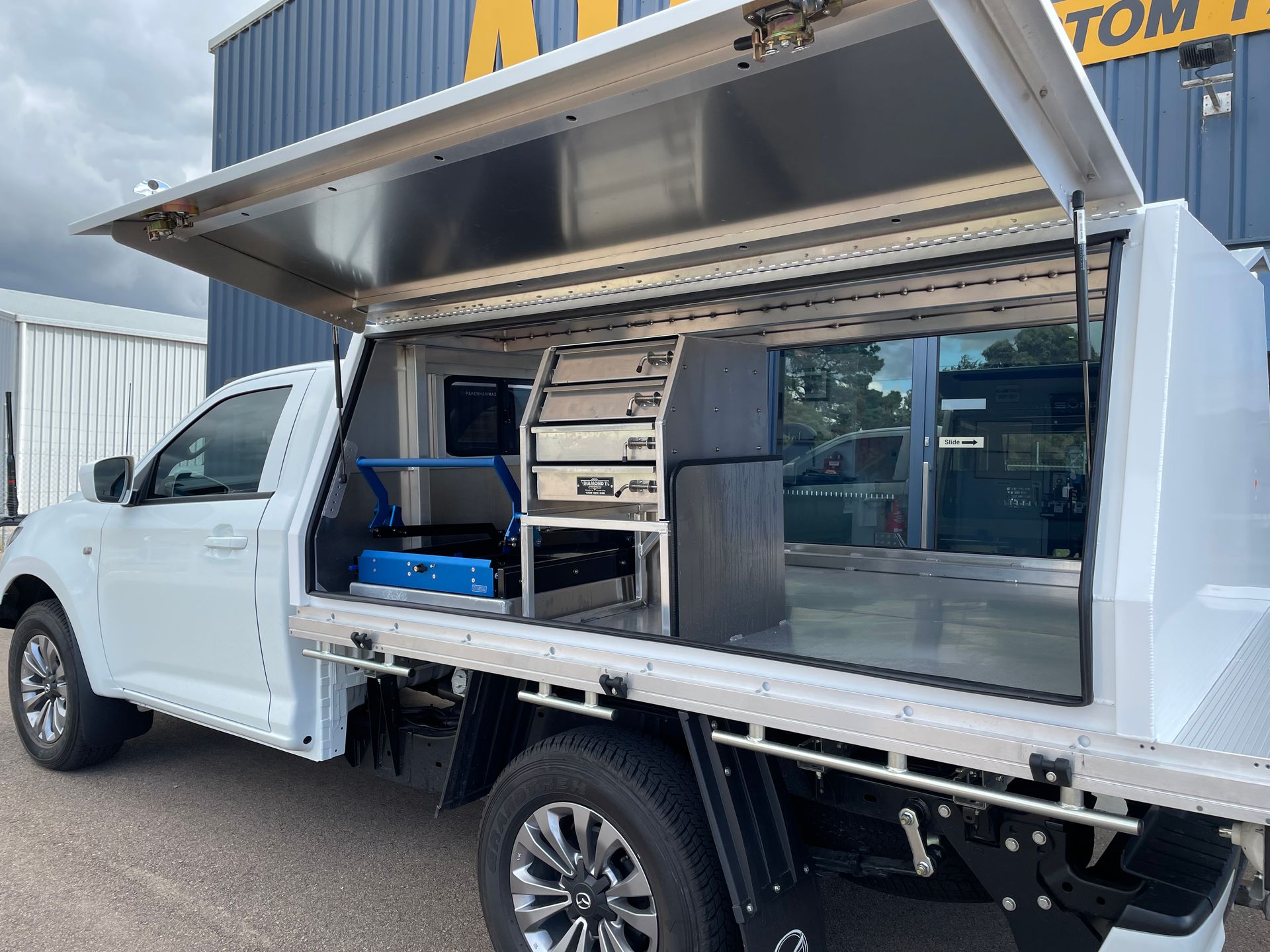 White truck with a utility canopy and open lid, revealing storage and equipment inside.
