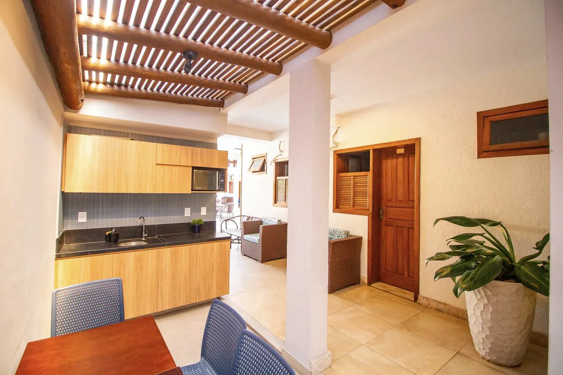 Cozinha e sala de jantar integradas, com armários de madeira, piso de cerâmica e vaso de planta junto a uma coluna branca.