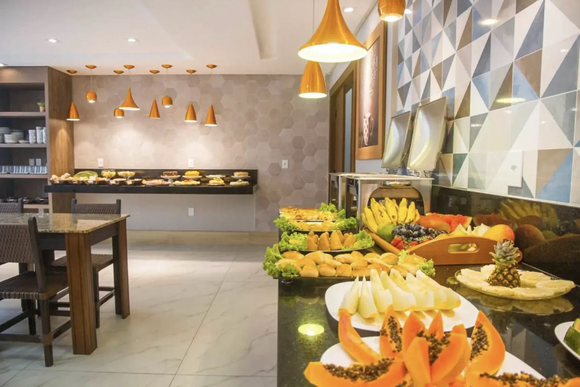 Buffet moderno com frutas frescas e sobremesas em uma sala de jantar com iluminação aconchegante.