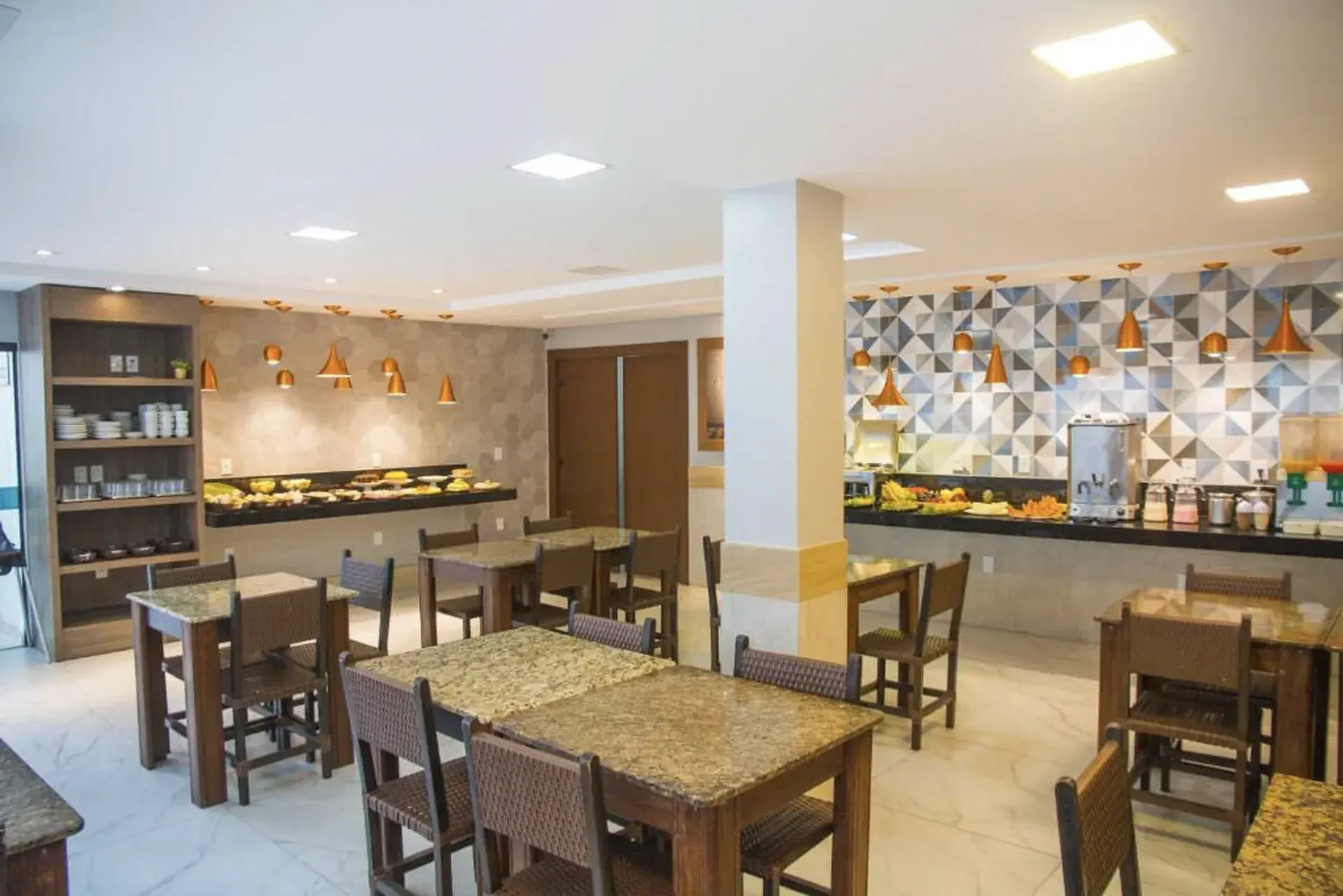 Sala de jantar moderna e iluminada com mesas e cadeiras de madeira, além de um balcão de buffet.