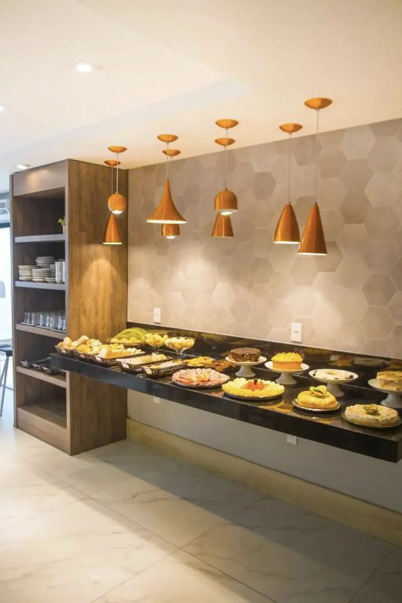 Balcão de buffet moderno com pratos variados sob luminárias pendentes de cobre em um restaurante.