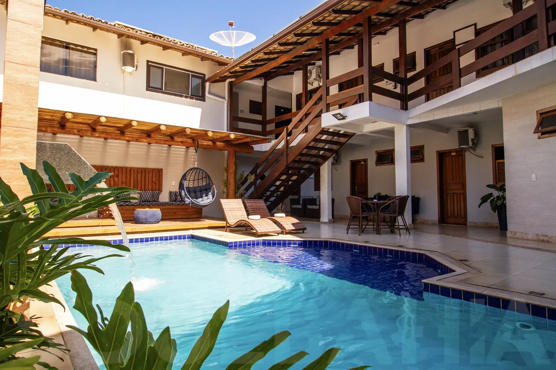 Piscina no pátio com espreguiçadeiras e varanda superior em uma villa ensolarada.