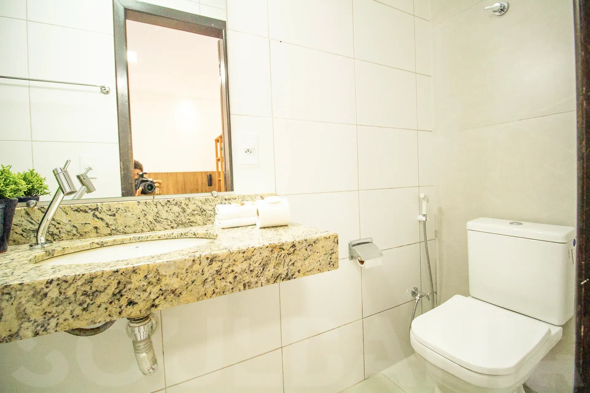 Pequeno banheiro revestido com azulejos, pia com bancada de granito, espelho e vaso sanitário branco.