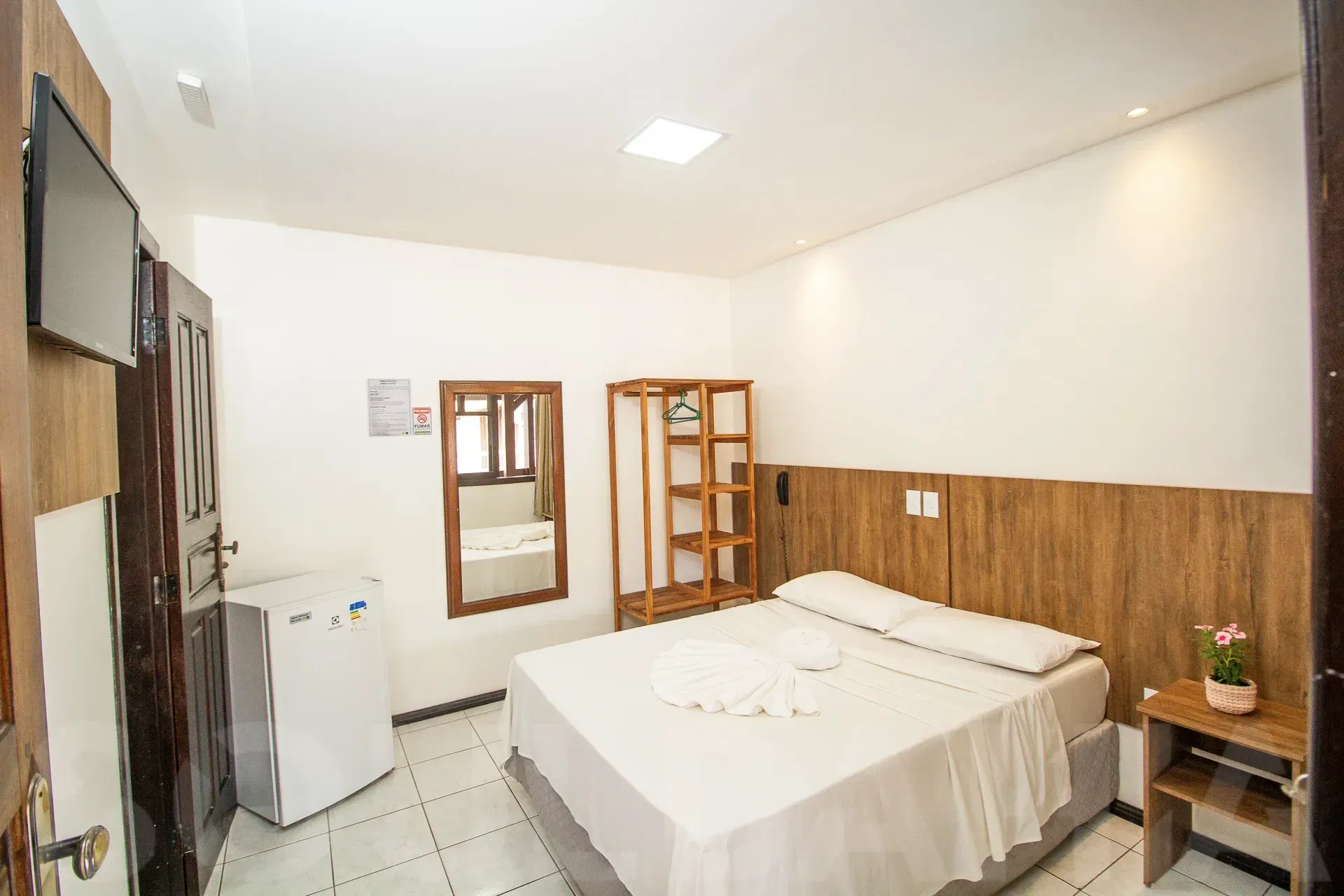 Quarto pequeno com cama de casal, painéis de madeira nas paredes, espelho na cômoda e paredes brancas.
