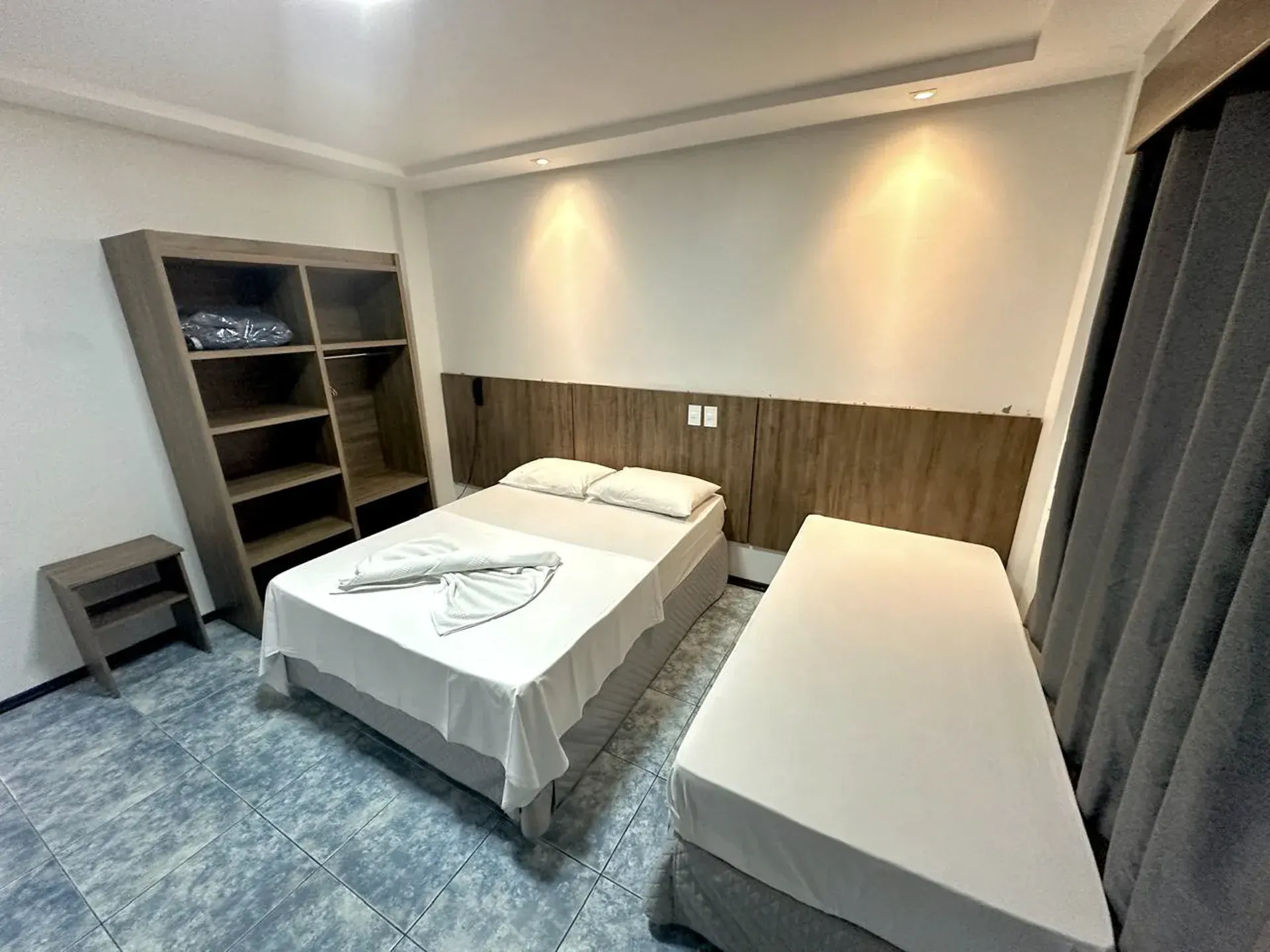 Quarto de hotel moderno com duas camas, carpete azul, parede com detalhes em madeira e cortinas.