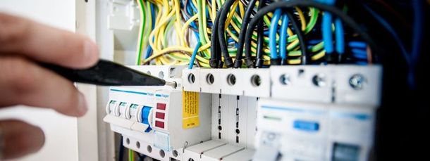 Mano che utilizza una sonda nera su un quadro elettrico con fili e componenti scoperti Efa Materiale Elettrico Massa (MS)
