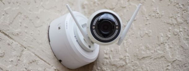 Telecamera di sicurezza bianca montata su una parete ruvida, angolata verso l'esterno e dotata di due antenne.
