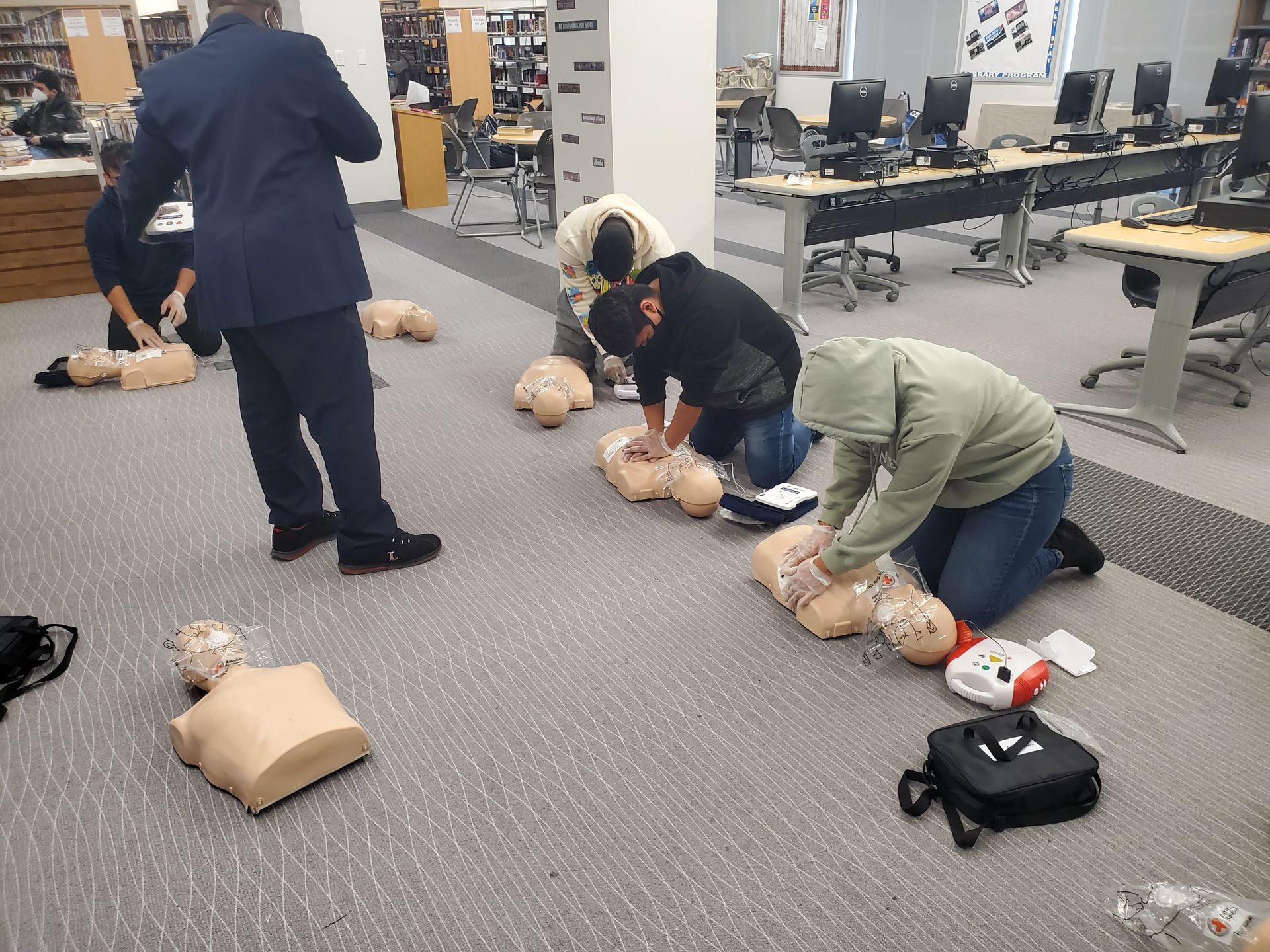 A group of people are practicing first aid on mannequins in a room.