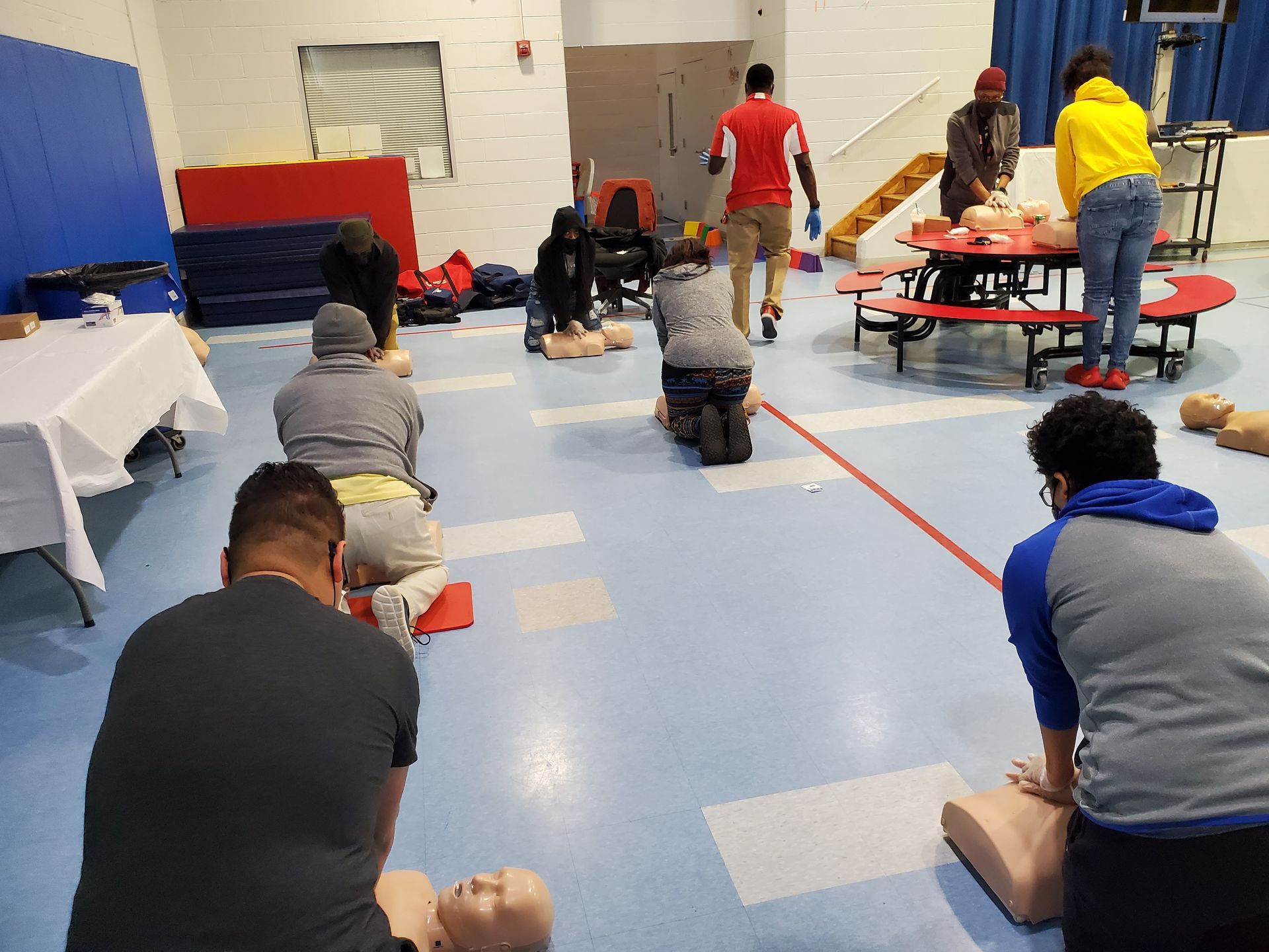 A group of people are practicing on a mannequin in a gym.