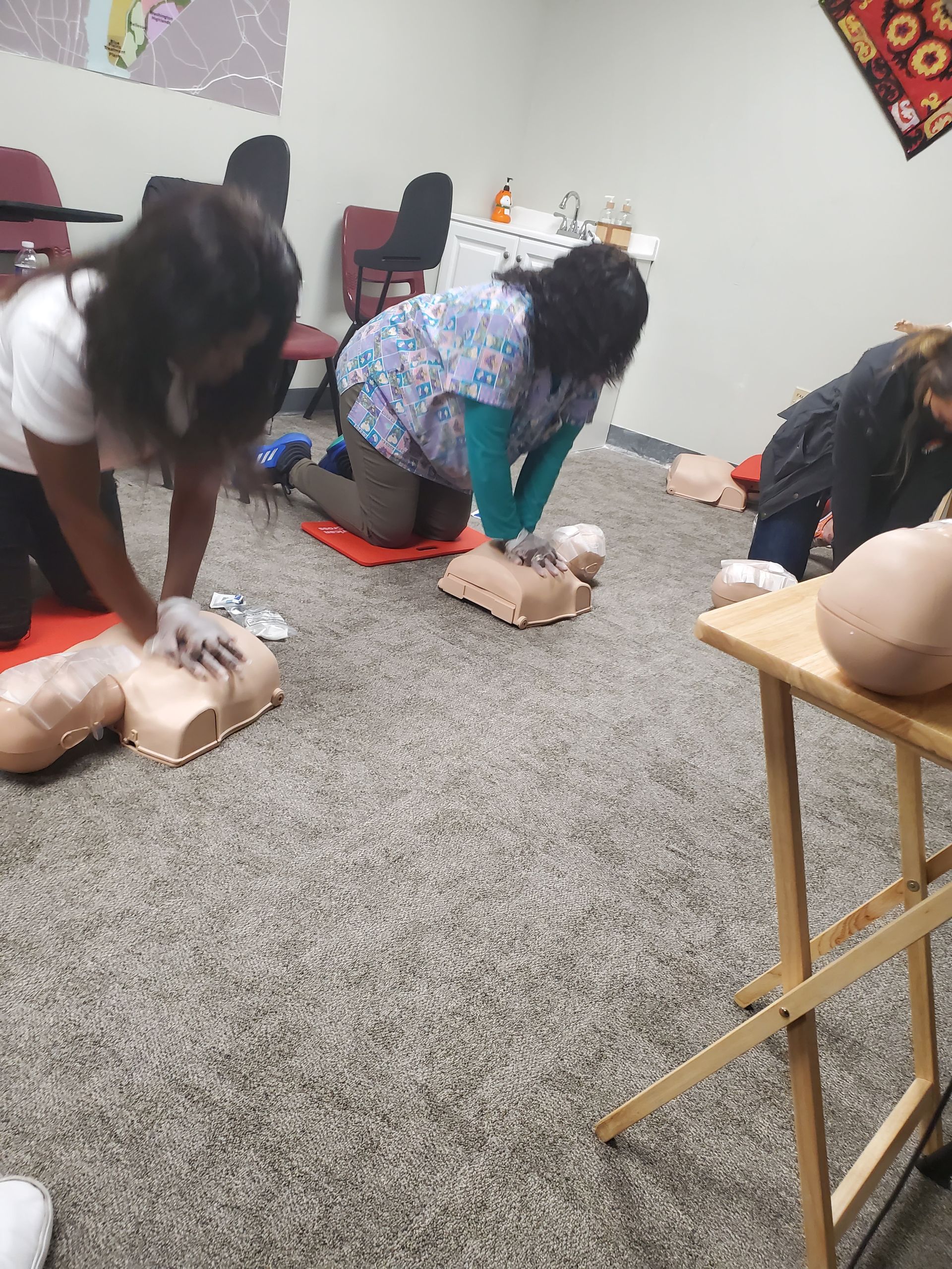 A group of people are kneeling on the floor doing a heart massage on a mannequin.