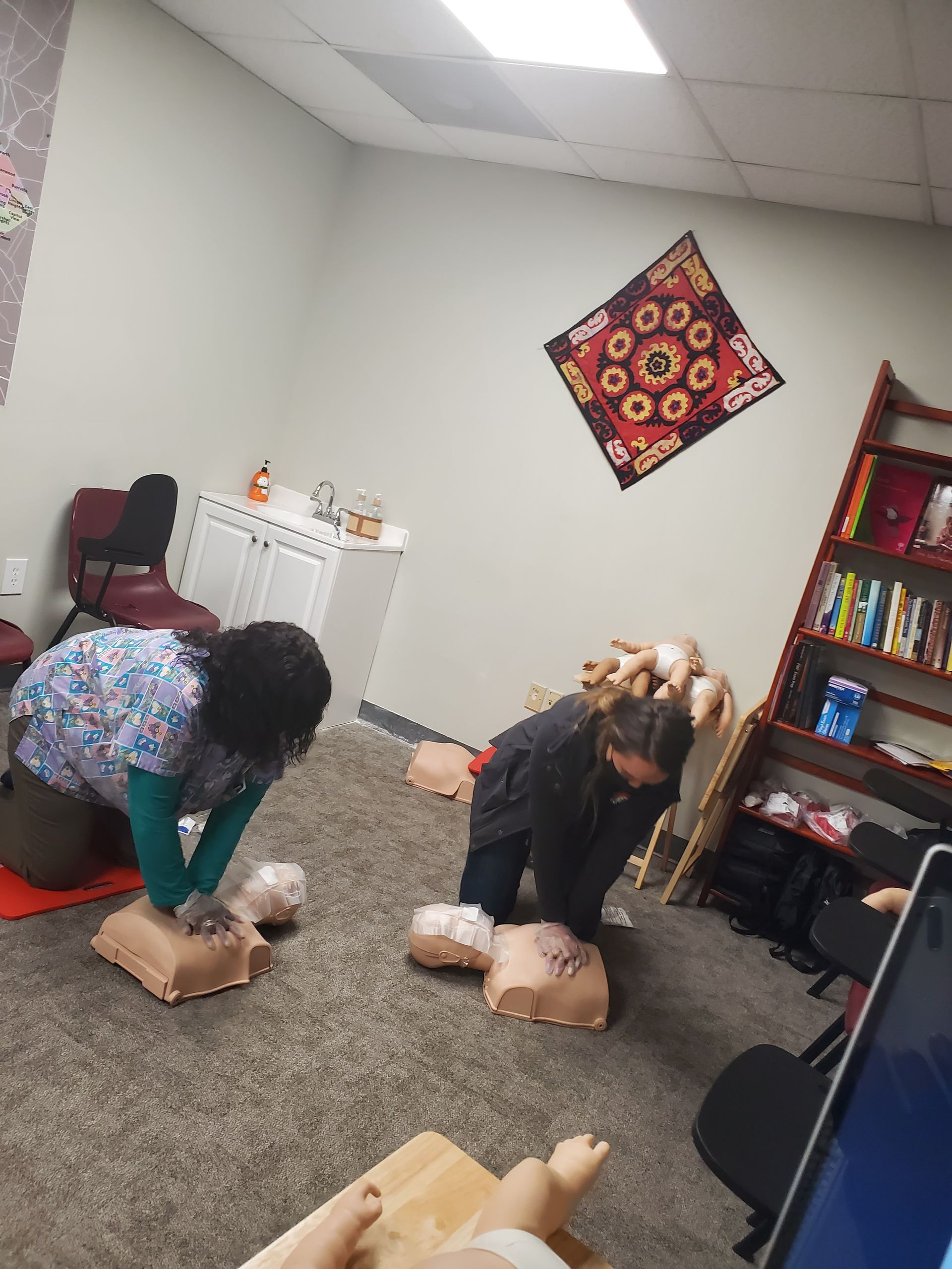 A group of people are practicing first aid on mannequins in a room.