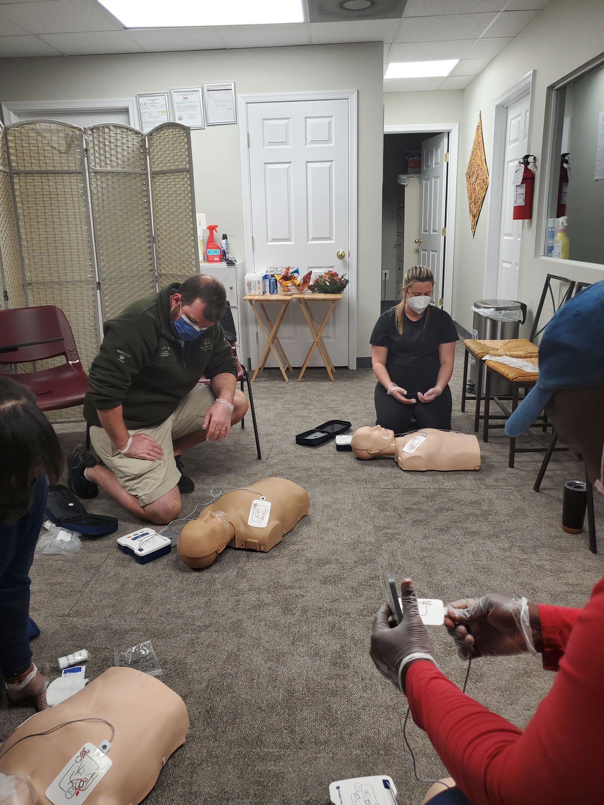 A group of people are kneeling around a mannequin in a room.