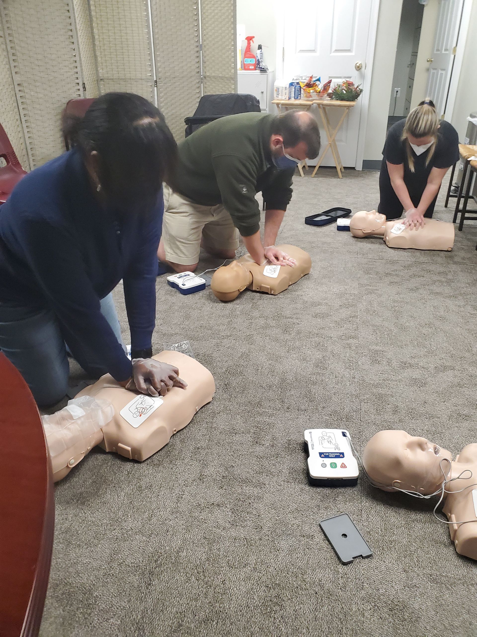 A group of people are practicing on a mannequin in a room.