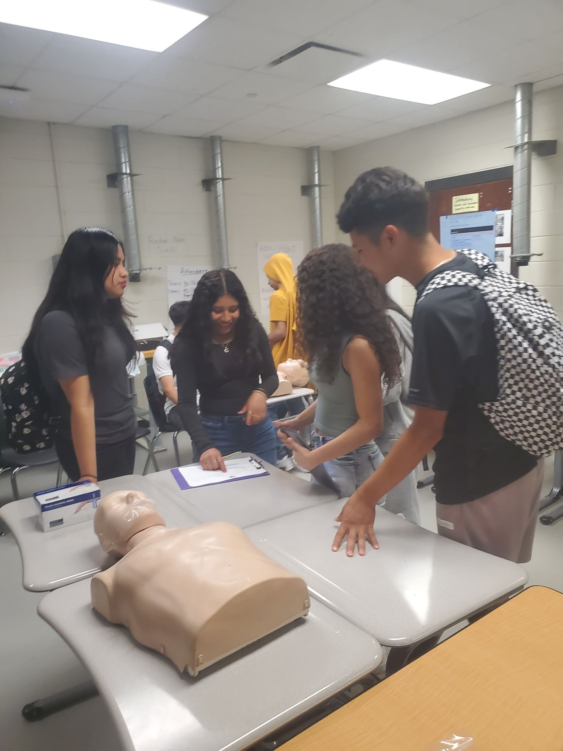 A group of people are standing around a table with a mannequin on it.