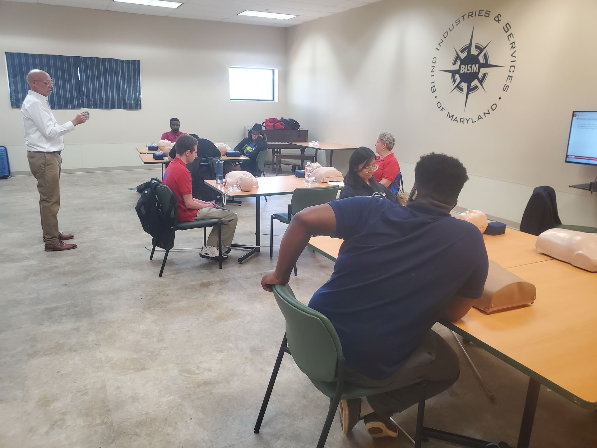 A group of people are sitting at tables in a room with a compass on the wall.