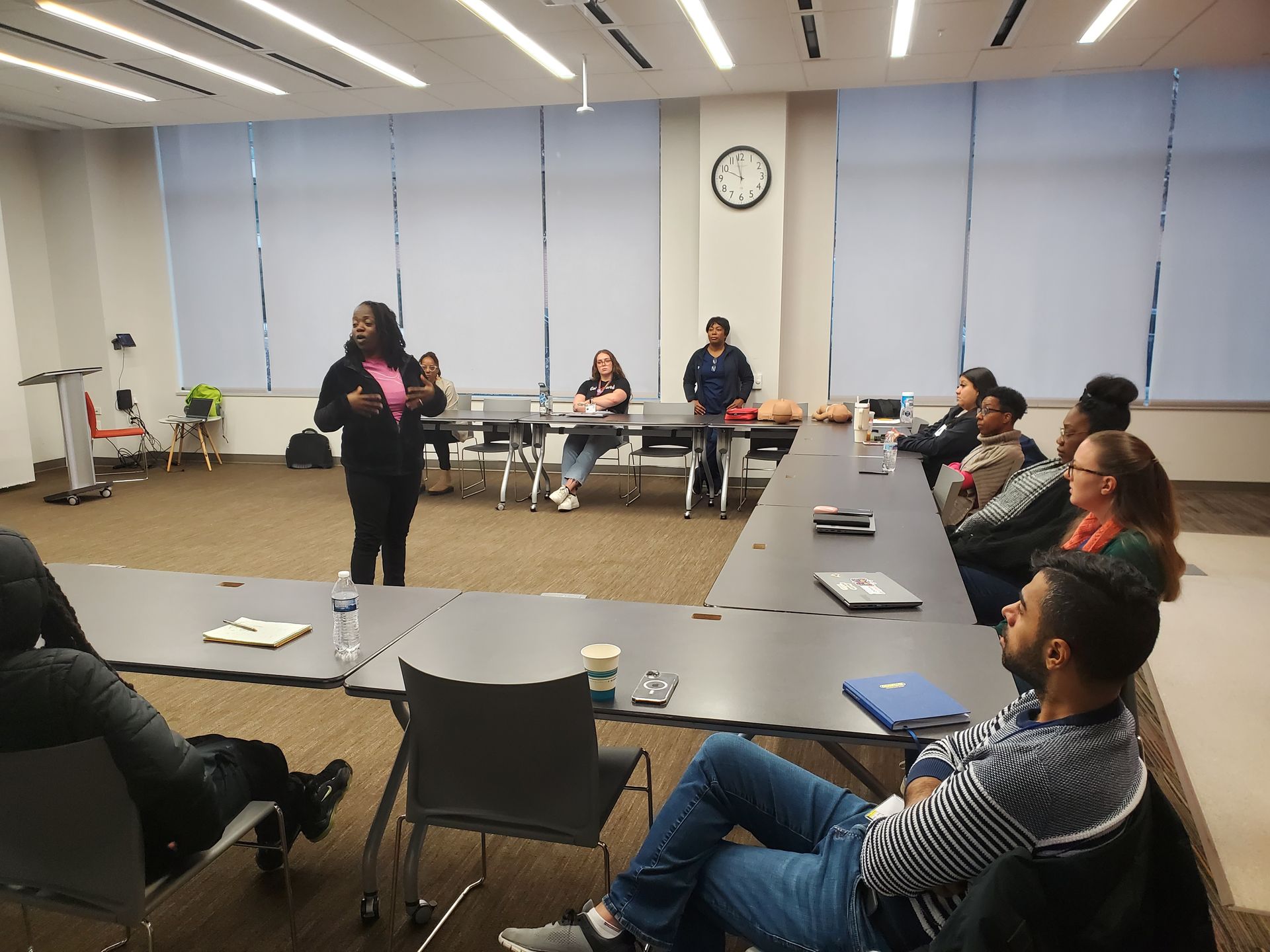 A woman is standing in front of a group of people sitting at tables in a conference room.