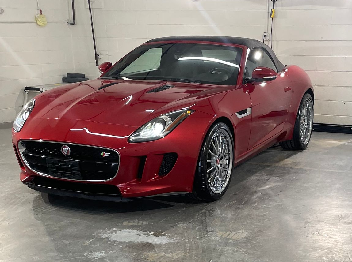 A glossy red Jaguar F-Type convertible parked in a bright, industrial garage setting.