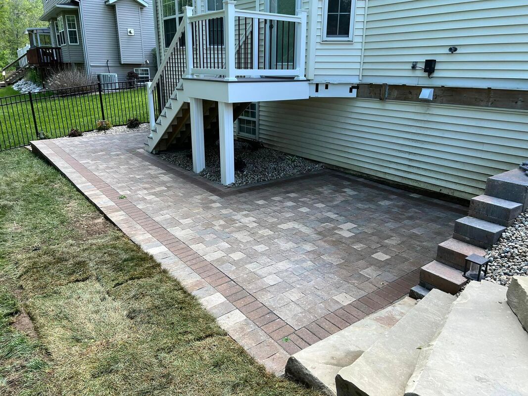 Backyard patio of brick pavers beside a house, with steps and a small raised deck