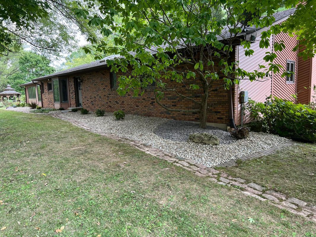 Brick house under leafy trees with a gravel border and grassy yard