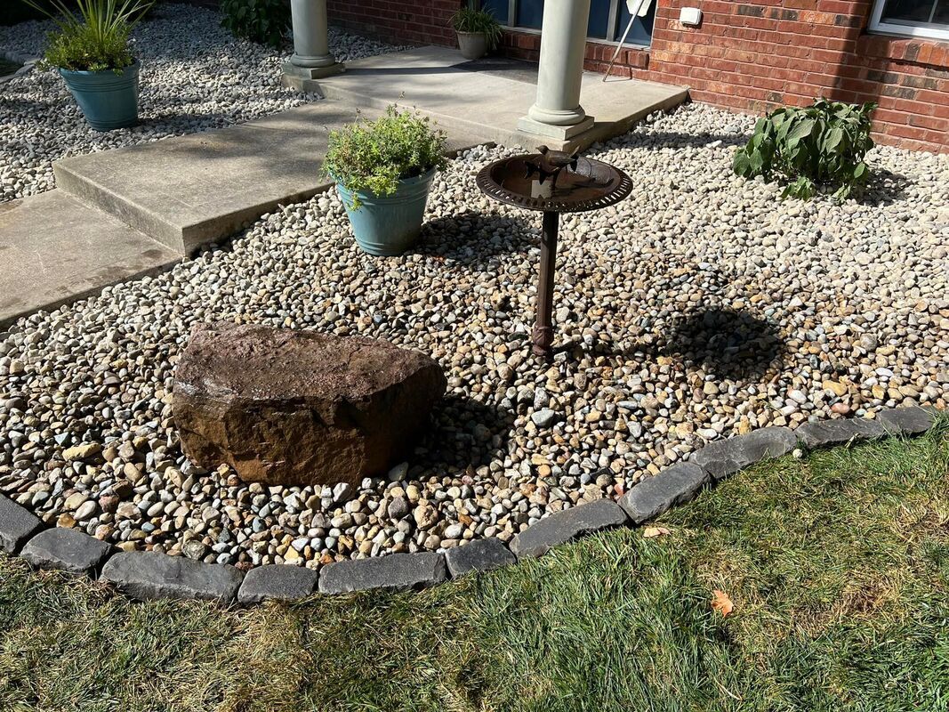 Rock garden with tree stumps, potted plants, and gravel border beside a lawn