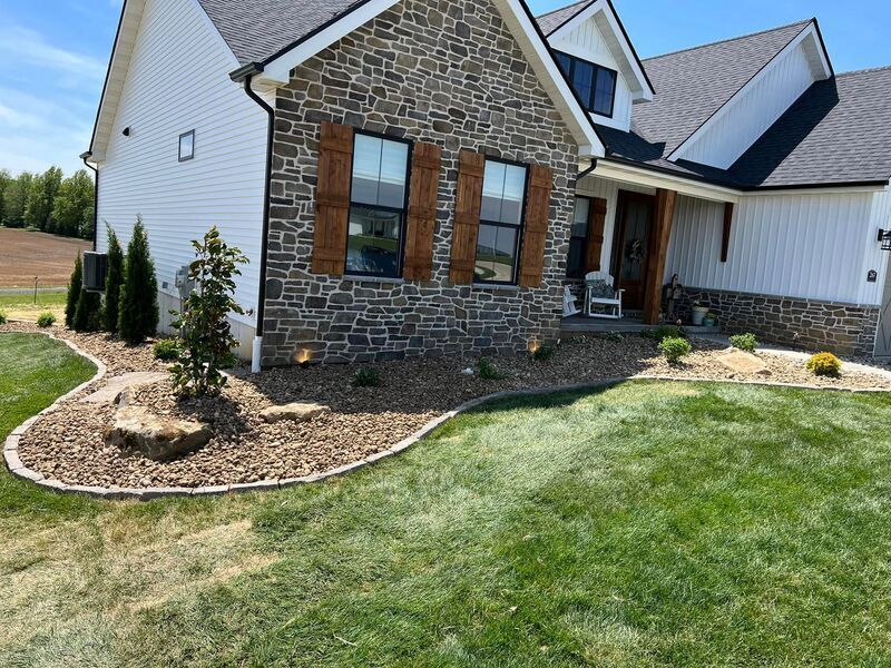 Stone and white suburban house with front porch, landscaped rock beds, and green lawn