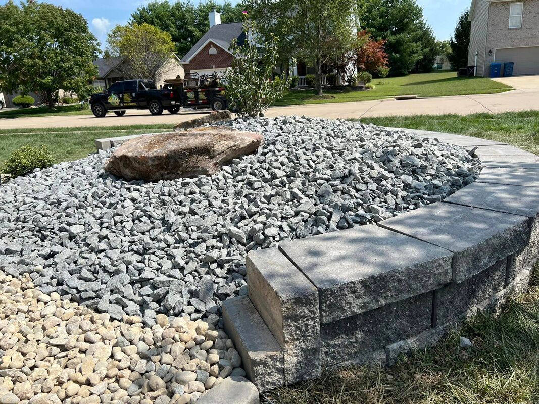 Stone landscaping retaining wall around a dry creek bed with white and gray rocks in a suburban yard