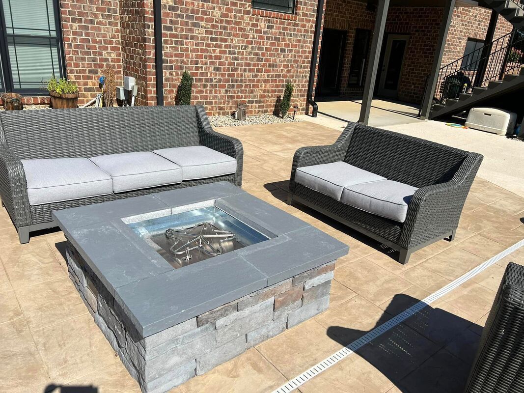 Patio seating area with two wicker sofas and a square fire pit table on a brick patio