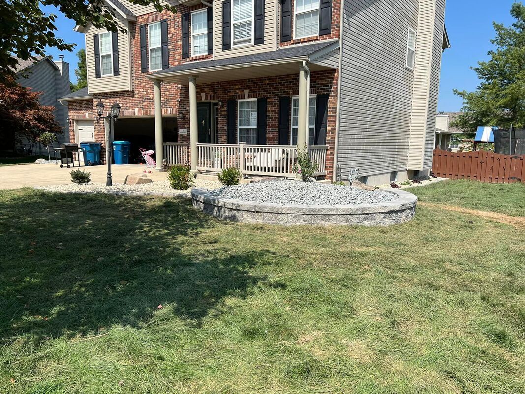 Two-story house with brick porch, stone landscaping, and a grassy front yard