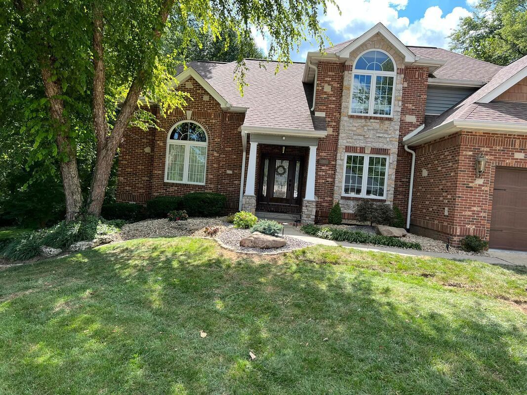 Brick house with a front porch, arched windows, and a green lawn under trees